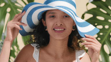Skincare model in white-blue sun hat applies sunscreen on cheeks