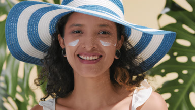 Beauty model in sun hat applies sun cream on her cheek