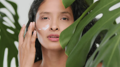 Young beautiful hispanic woman applying cream on her cheek