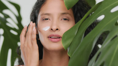 Young positive hispanic woman applies face cream on her cheek